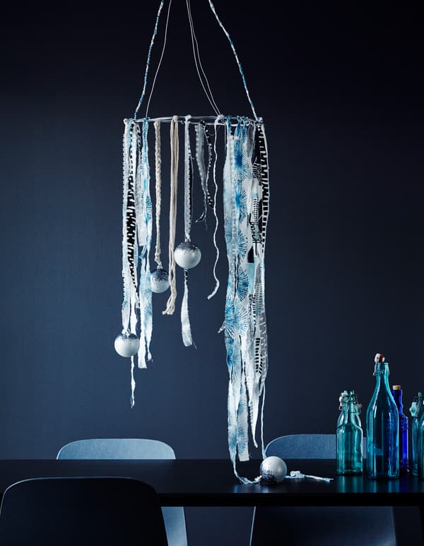 A decoration made with strips of blue-white textiles and baubles hanging from a circular wire suspended over a table.