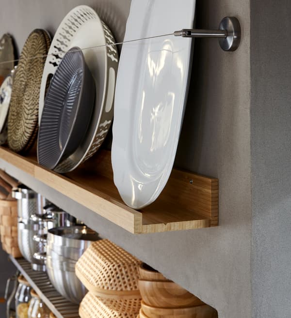 A decorative storage wall with a wooden picture ledge displaying dishes and trays, all in white, grey and brownish tones.