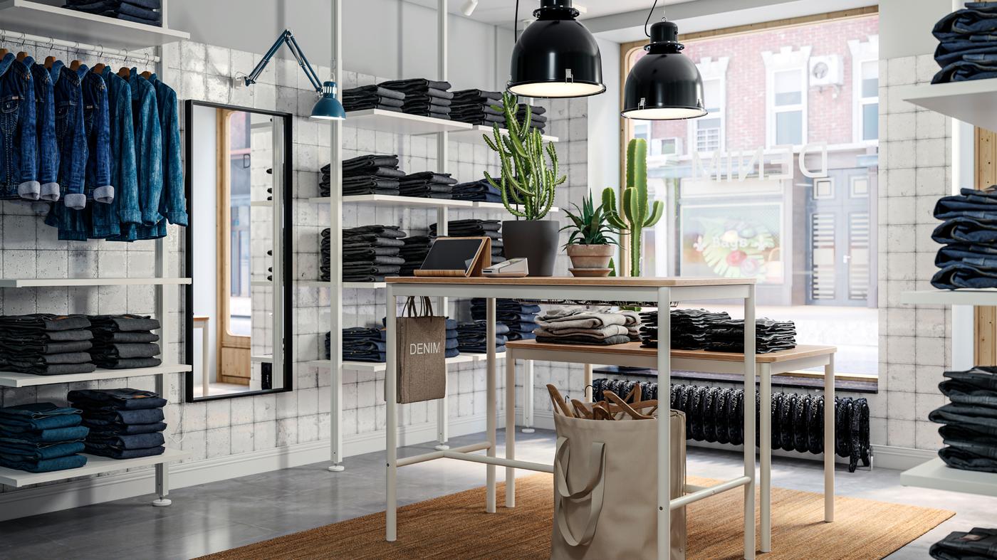 A denim-store interior with stacks of folded jeans and other garments on ELVARLI storage combinations and TOMMARYD tables.
