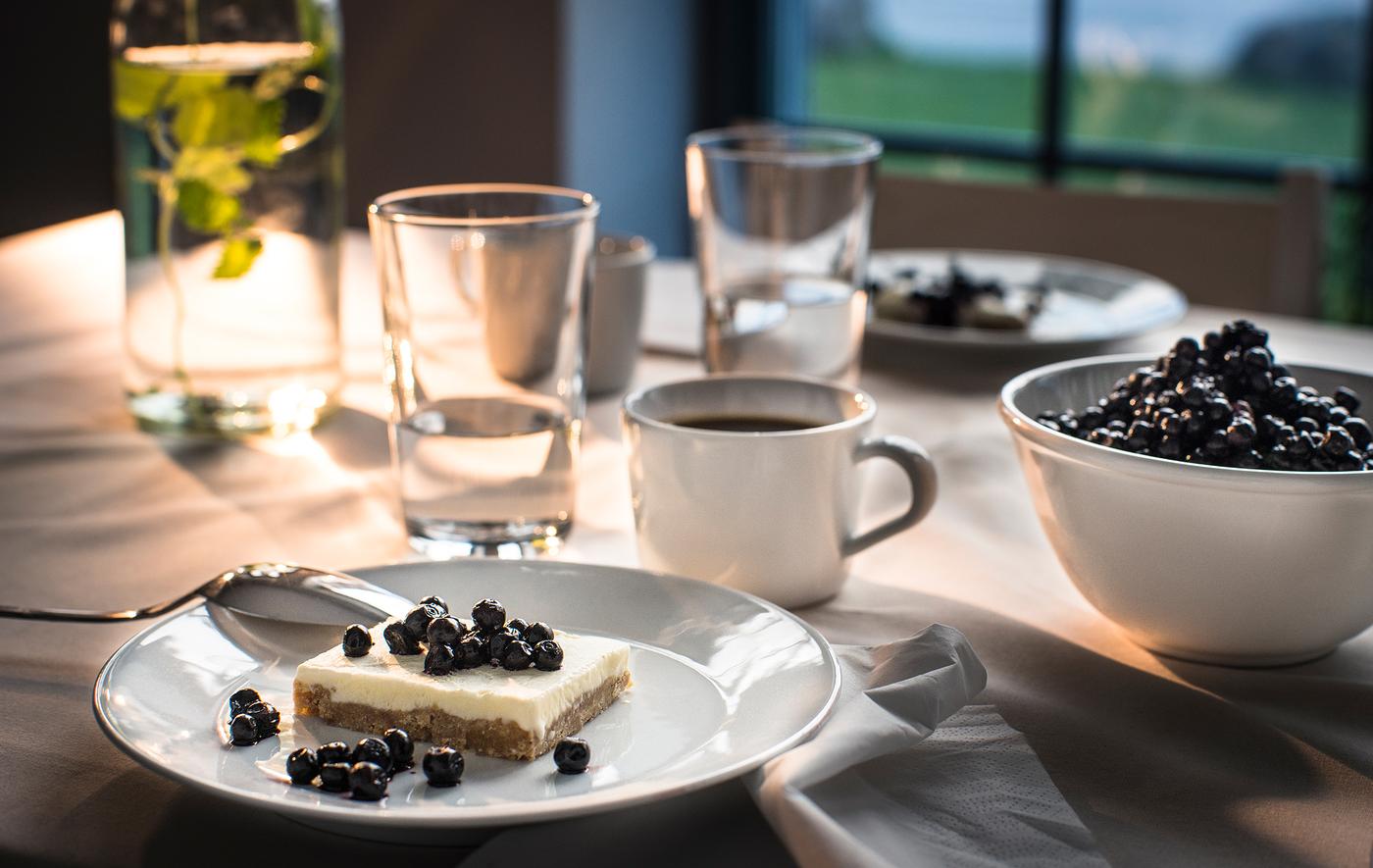 A desert plate boasting a cake with fresh berries, set at a table with coffee and other dishware.
