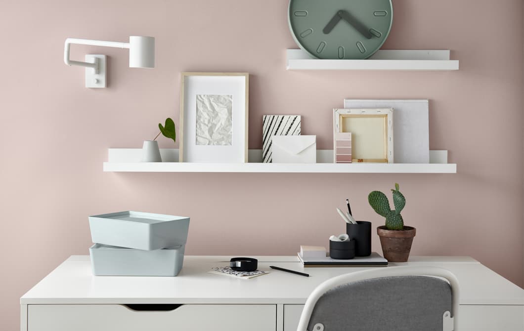 A desk, drawer and chair in a home office set against a wall decorated with big splatters of different coloured paint.