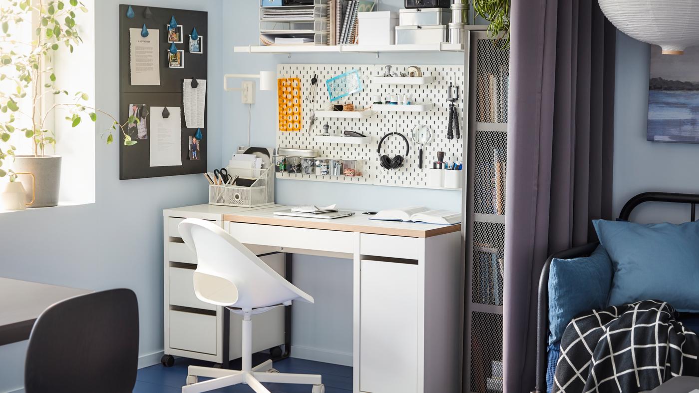 A desk, swivel chair, wall-mounted shelf and a pegboard in white, a grey cabinet and a window.