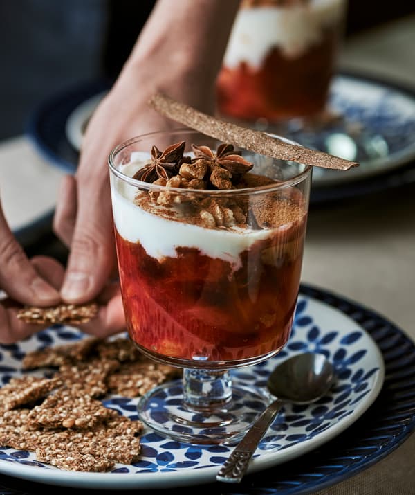 A dessert glass filled with winter stewed fruit and yogurt, set on a blue flower-patterned plate.