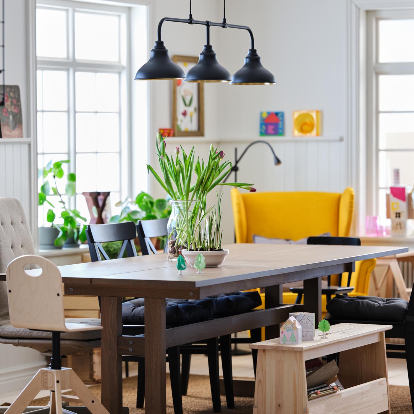A dining area with a table, chairs and lamps in a large, light and airy room.