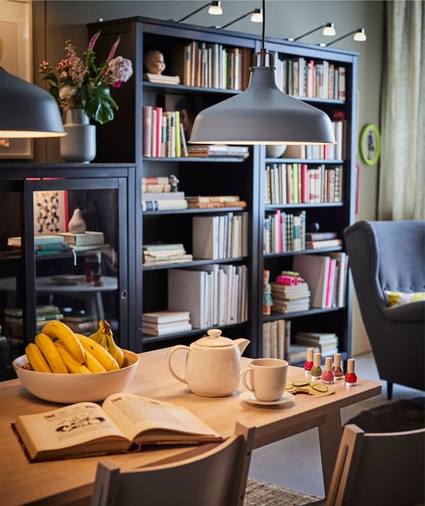 A dining area with an IKEA RANARP pendant lamp illuminating the table, with bookcases behind.