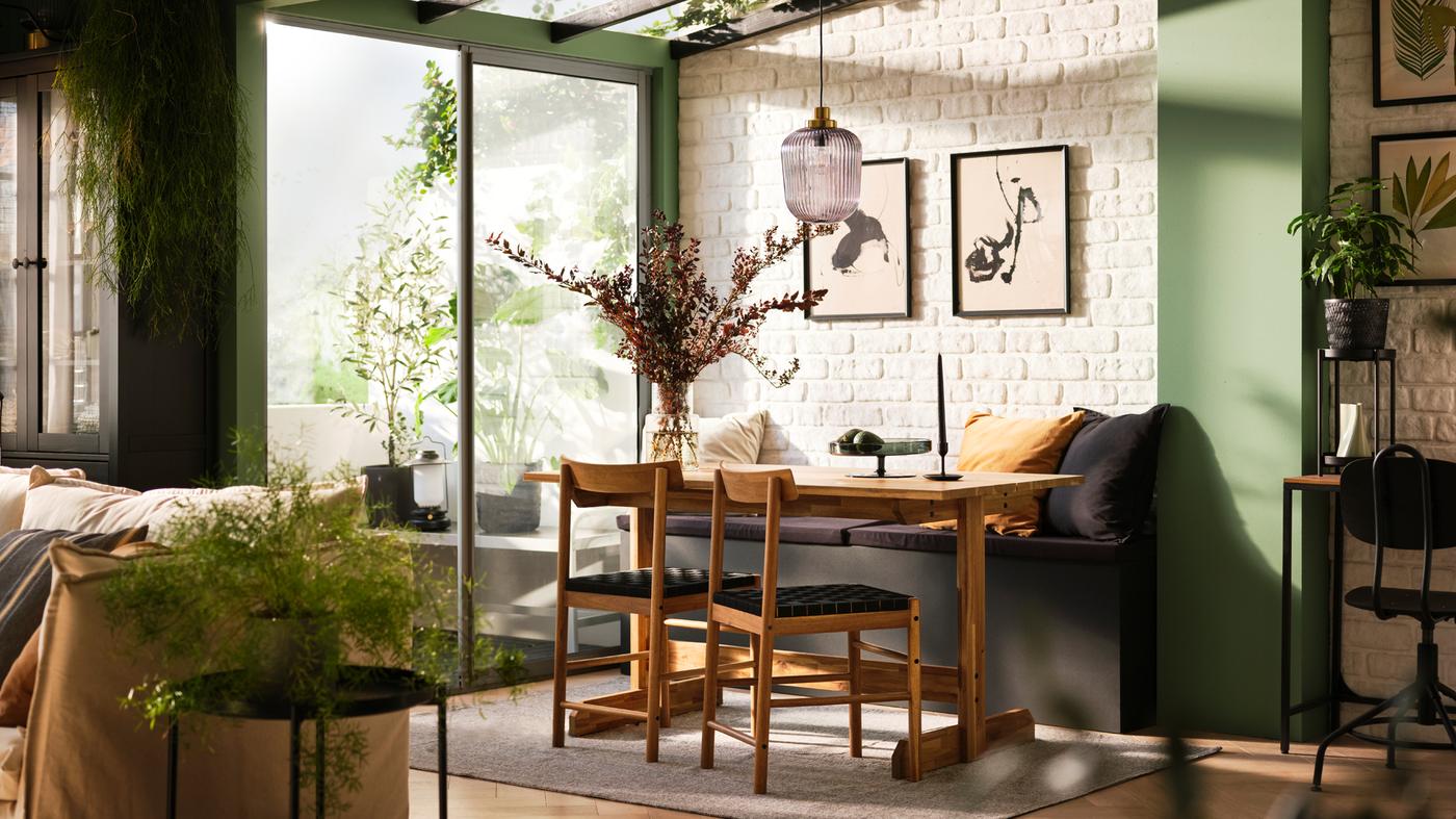 A dining room containing lots of plants and a NACKANÄS dining table and chairs in front of a bench and beside a patio door.