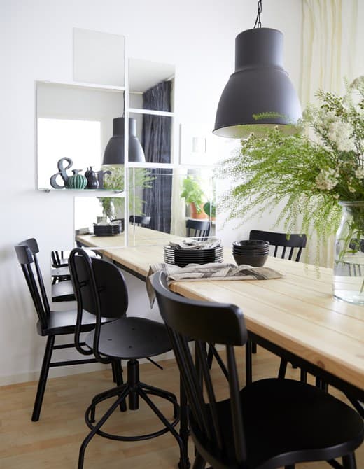 A dining room with a pine table and six black chairs and a wall decorated with mirrors to help create depth in the room.