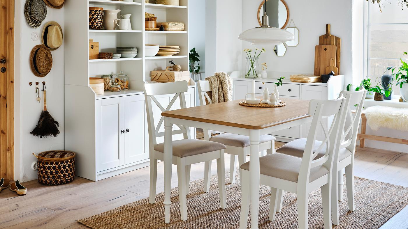 A dining room with a table in oak/white, four white chairs, a jute rug and two white high cabinets with two doors each.