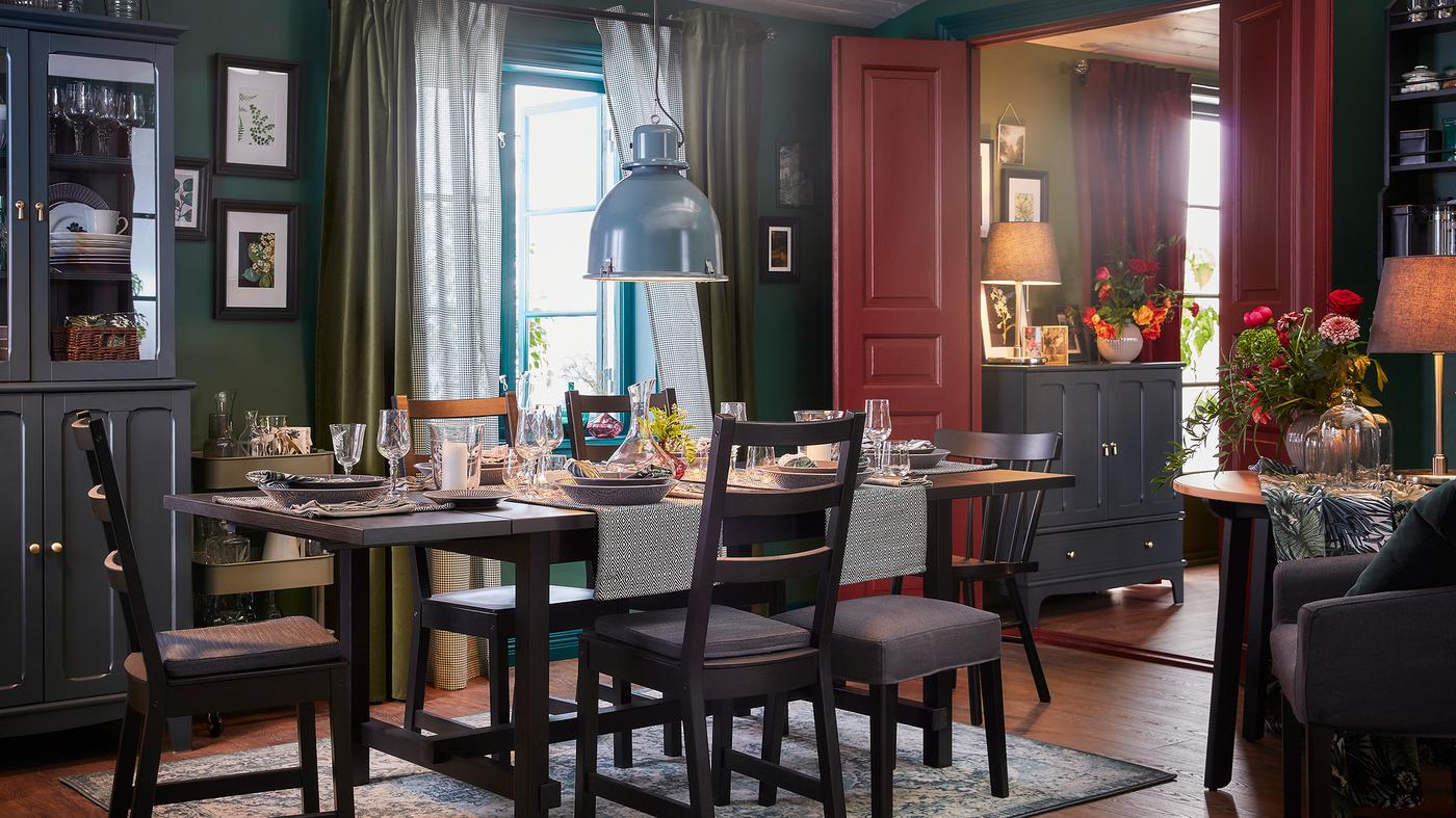 A dining room with an table and five chairs in black, an oriental-patterned rug and a grey-turquoise pendant lamp.