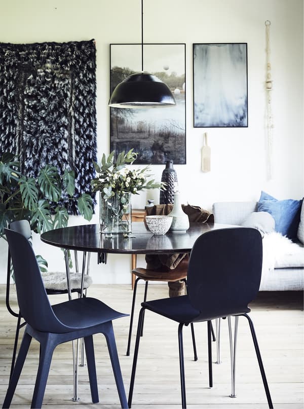 A dining room with pictures, wall hanging and pendant light.