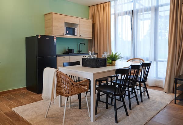 A dining setting featuring a white table, woven and black chairs with a kitchenette placed against the wall.
