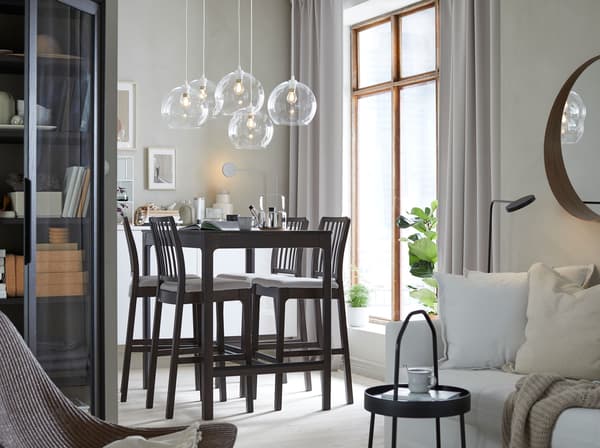 A dining space with EKEDALEN dark brown four-seater bar table and high bar stools and JAKOBSBYN clear glass pendant lampshades.