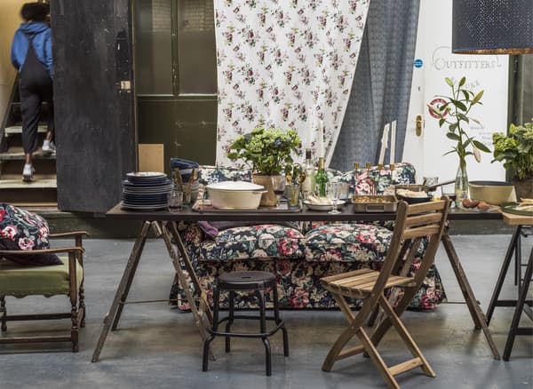 A dining space with mismatched chairs, potted plants and a floral sofa.