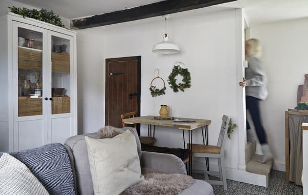 A dining table, cabinet and sofa in neutral colours, in a small cottage.