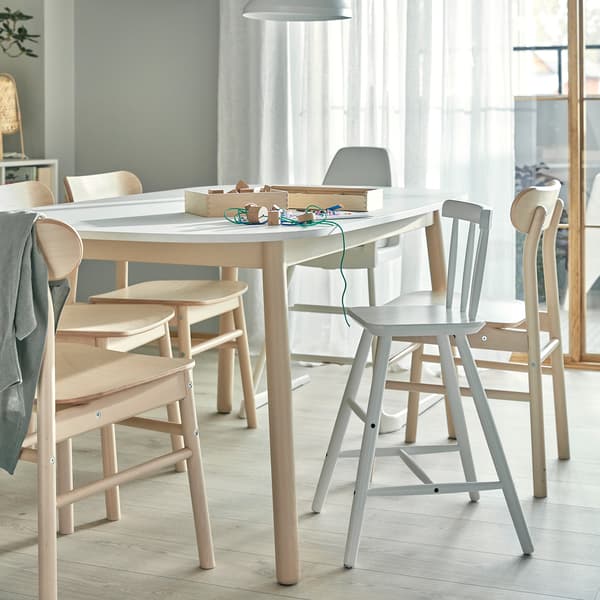 A dining table, chairs in birch, a highchair and a junior chair with feet support. Children's crafts lie on the table.