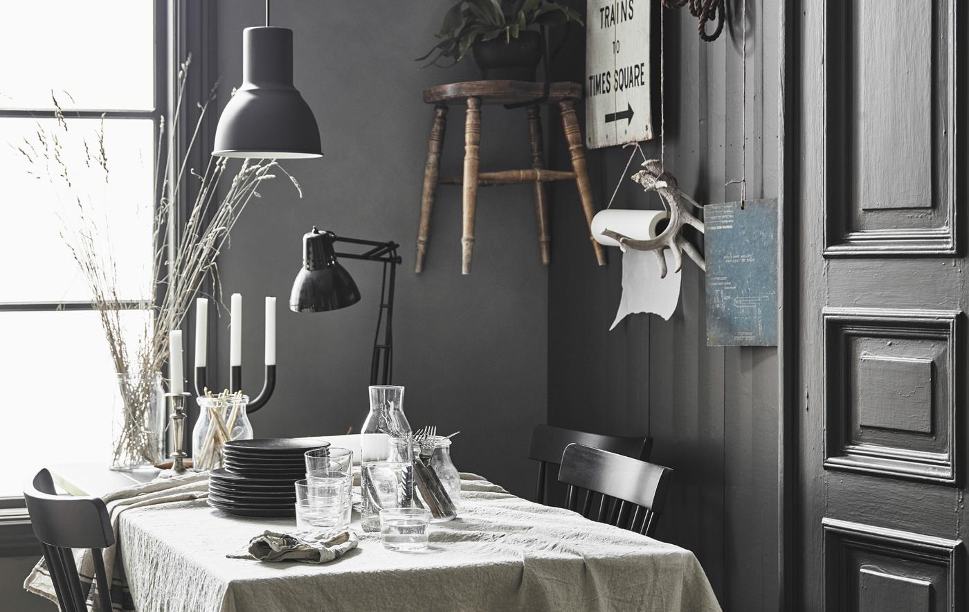 A dining table covered in a linen table cloth in a modern rustic kitchen with personal decor hanging on a wall