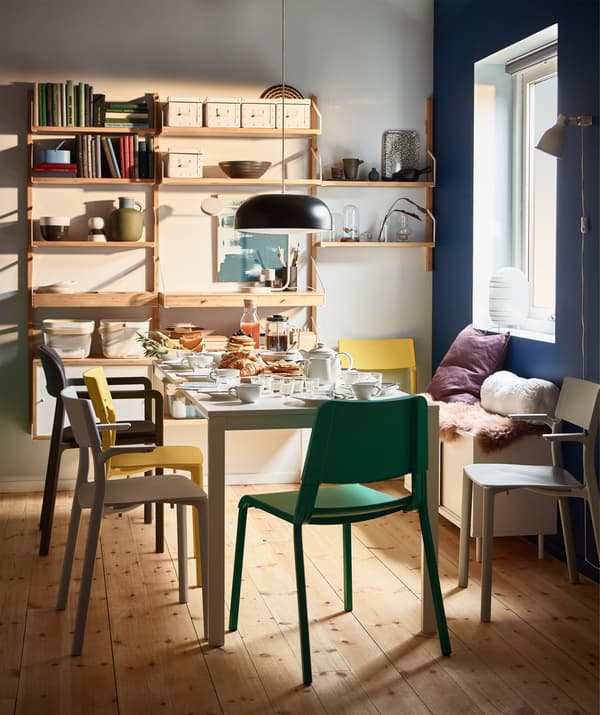 A dining table that has been set for breakfast, surrounded by colourful JANINGE stackable chairs.