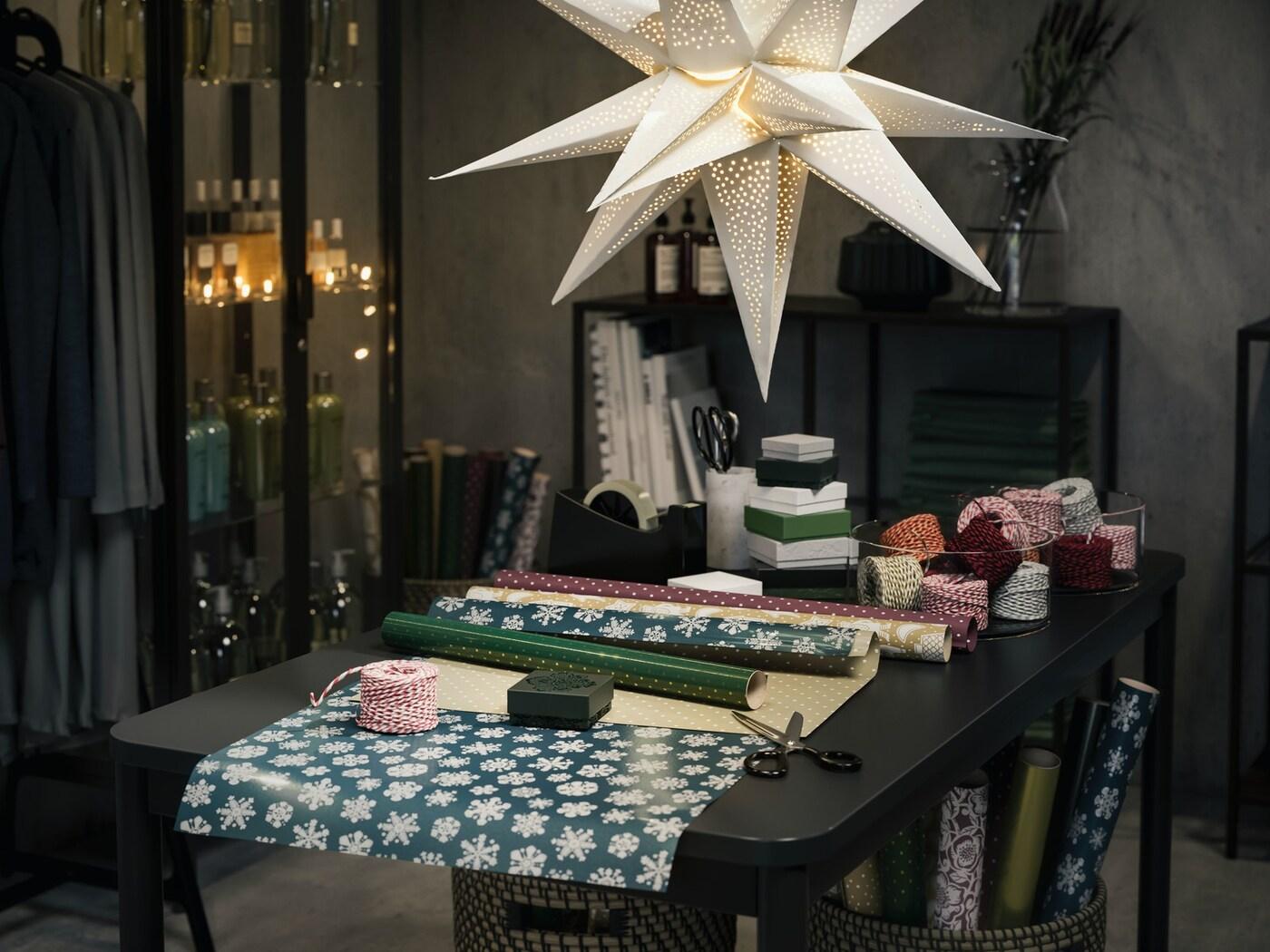A dining table with a star hanging lamp above and table filled with beautiful wrapping paper and ribbon