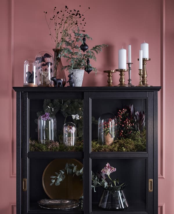 A display cabinet is decorated and filled with greenery, flowers and glass domes.
