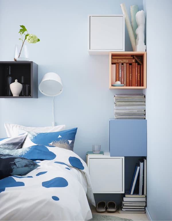 A DIY bedside table setup made from colourful cubic cabinets secured to the walls around a bed.