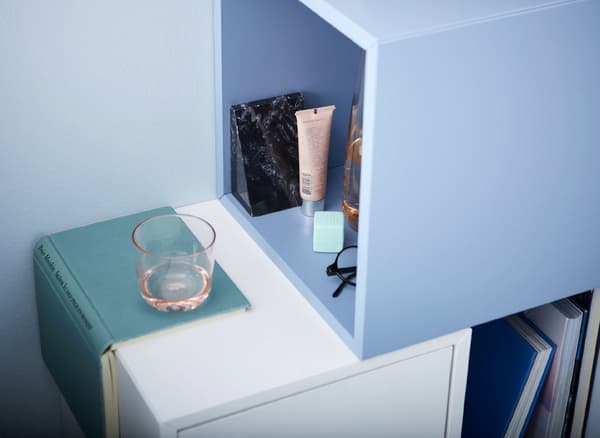 A DIY bedside table setup made of cubic cabinets that hold some cosmetic tubes, a pair of spectacles and a glass.