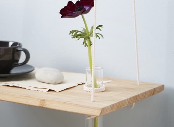A DIY hanging bedside table made from a chopping board with a cup and a flower in a glass vase.