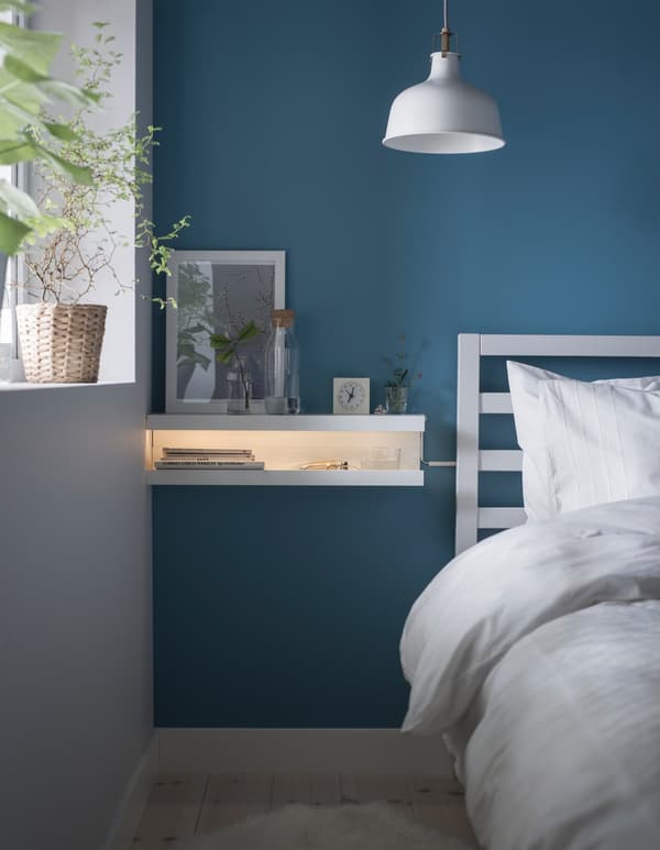 A DIY nightstand made from two MOSSLANDA picture ledges mounted on a blue wall in a bedroom.