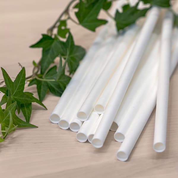 A dozen white IKEA paper straws lying on a wooden bench.