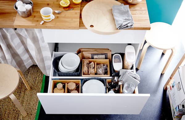 A drawer filled with containers of dry food stuff, bowls, plates, cutlery and glasses 