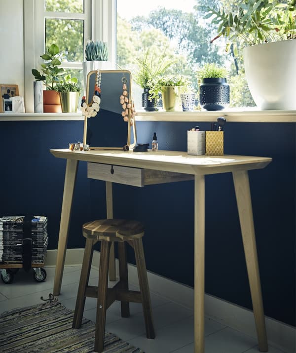 A dressing table and stool against a blue wall under a window.