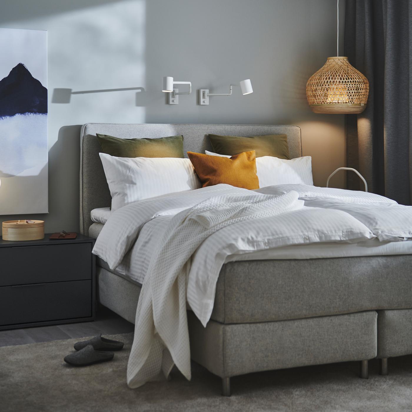 A DUNVIK divan bed with white NATTJASMIN bed linen stands in a bedroom near a bamboo MISTERHULT pendant lamp.