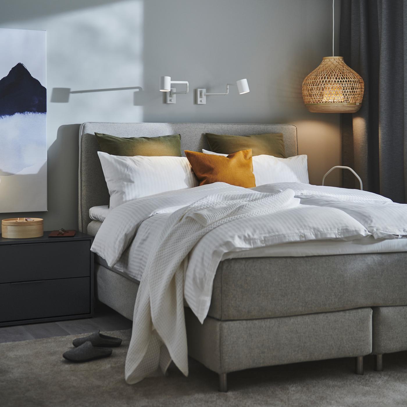 A DUNVIK divan bed with white NATTJASMIN bed linen stands in a bedroom near a bamboo MISTERHULT pendant lamp.