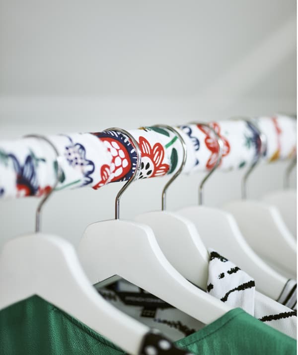 A fabric-wrapped clothes rail with white hangers for clothes.