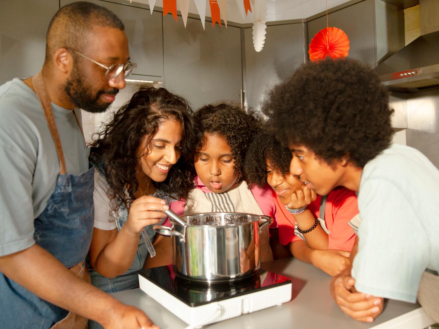 A family of five is stirring an IKEA 365+ pot on a TILLREDA portable induction hob.
