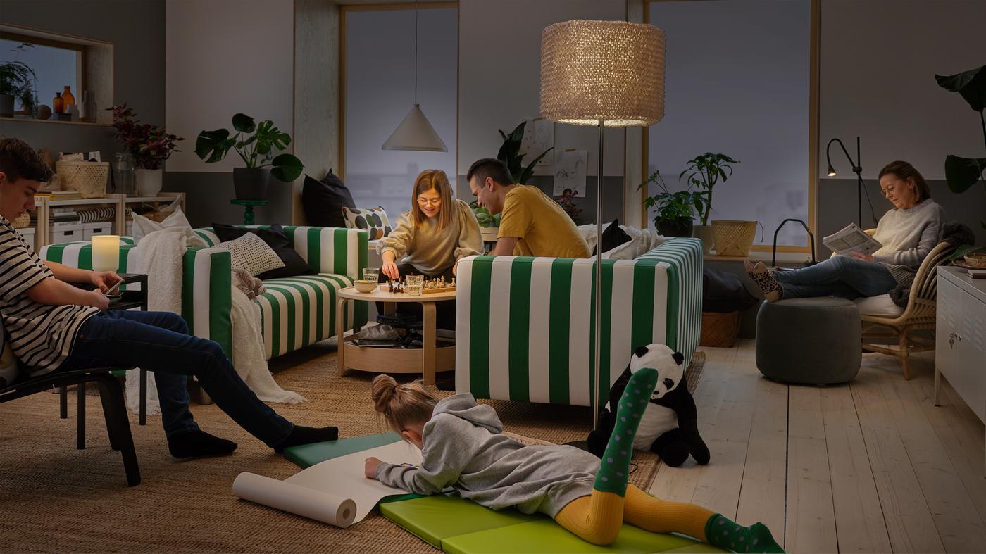 A family spend time together at home. NÄVLINGE pendant lamp, ISBRYTARE table lamp and NÄVLINGE floor lamp brighten the room.