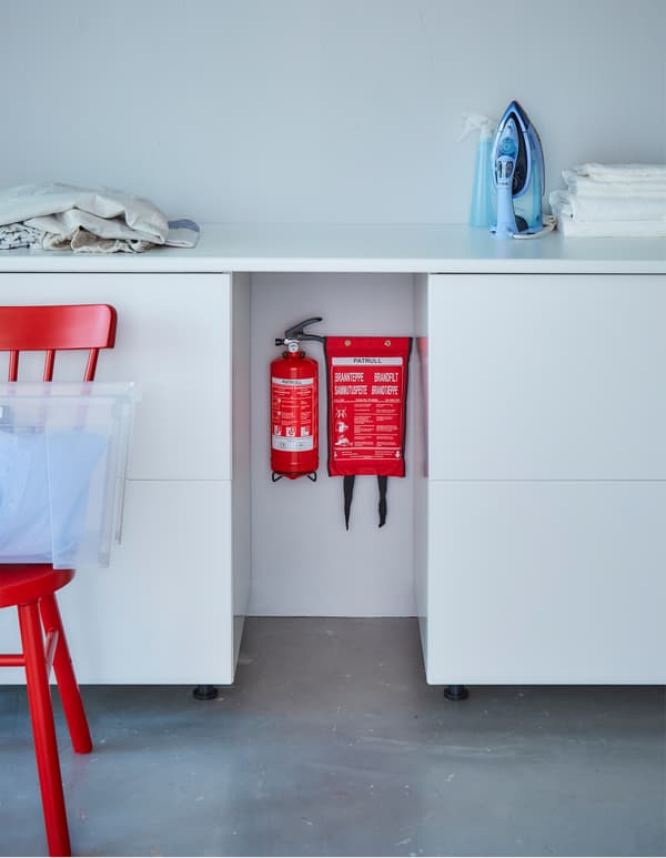 A fire extinguisher and fire blanket are hung on a wall between two cabinets.