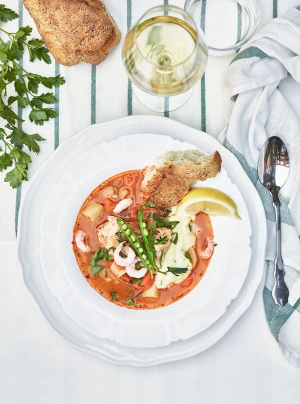 A fish stew, piece of bread and a glass of wine are shot from above.