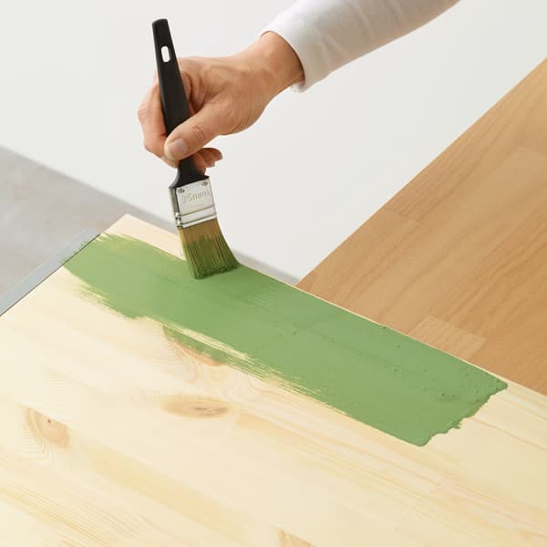 A FIXA paintbrush used to hand paint a wooden surface in green