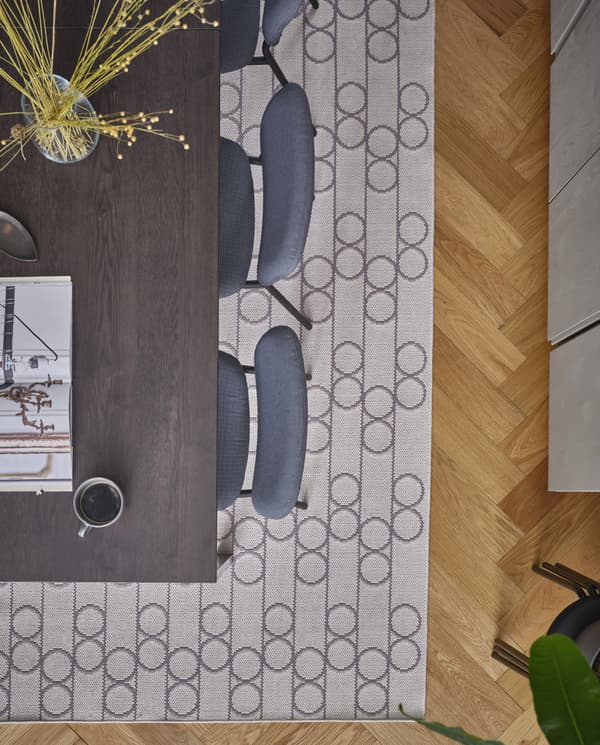 A flatwoven rug with a geometric pattern with circles lies beneath a black/dark brown dining table and grey chairs.
