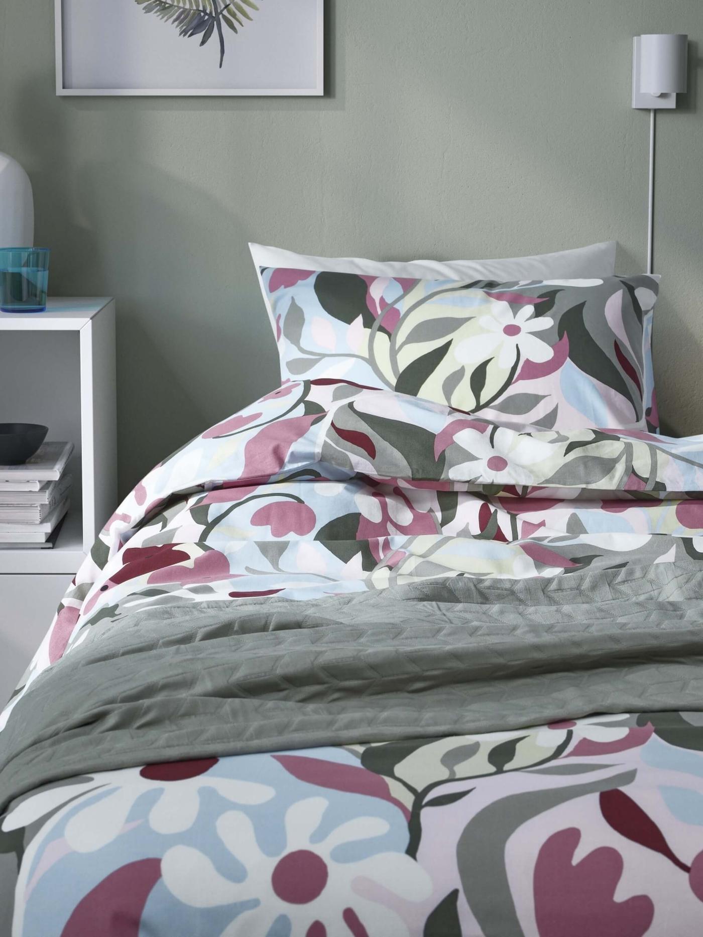 A floral bedding with maroon and blue shades in front of a green background.