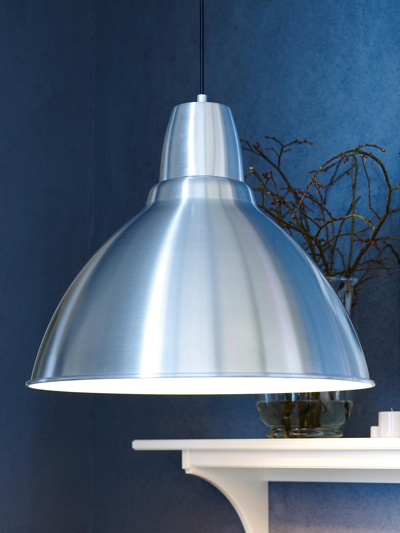 A FOTO pendant lamp hanging in a room with blue walls and a white wooden mantlepiece, upon which are branches in a vase.