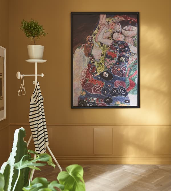 A framed piece of artwork is hung on an ochre wall, with a valet stand in the corner.