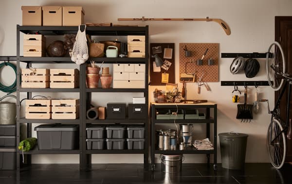 A garage wall with a black BROR shelving unit, filled with wooden, cardboard and plastic boxes in different sizes.