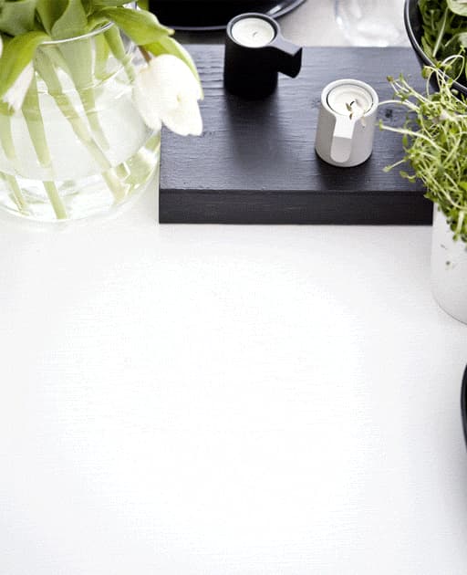A gif of a monochrome place setting with green napkin, flowers in a vase and herbs in a white pot.