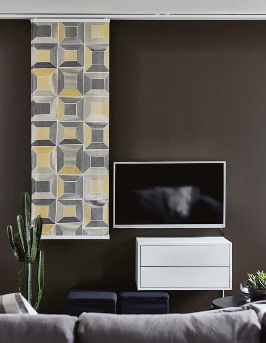 A GIF of patterned IKEA panel curtains sliding in front of a TV to hide it in this living room.