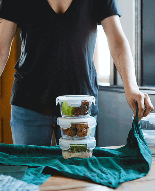 A GIF of someone using a green tea towel to tie up a takeaway lunch packed in three glass containers.
