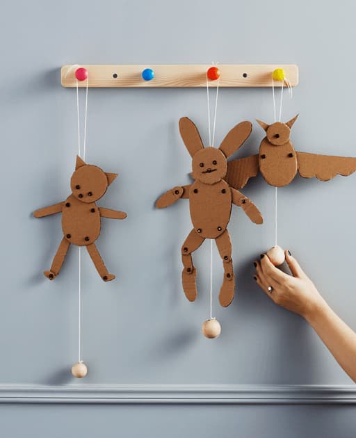 A GIF of three handmade cardboard toys hang from hooks on a wall.