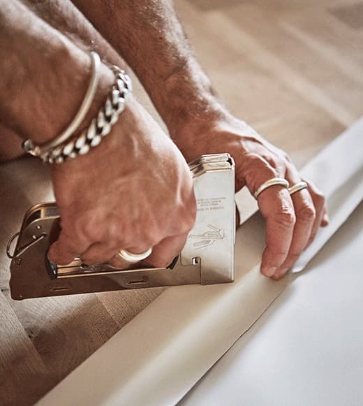 A GIF shows a man fitting and stapling the roller blind to the wooden canvas.