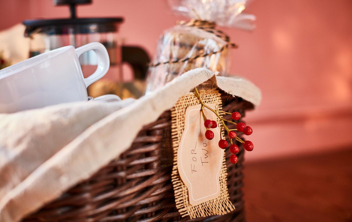 A gift-style basket with a cellophane-wrapped stack of biscuits, cups, a cafetière and decorations.