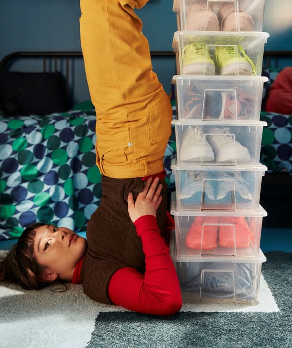 A girl balancing on her back against a stack of SAMLA boxes containing colourful sneakers.